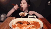 a woman is eating noodles with chopsticks from a large plate