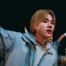 a young man with blonde hair is wearing a light blue jacket
