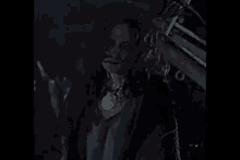 a woman with red hair is standing in a dark room with a necklace around her neck .