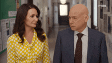 a man in a suit and tie stands next to a woman in a yellow shirt with max on the bottom right