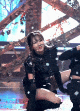 a woman in a black outfit is kneeling down on a stage with confetti falling around her