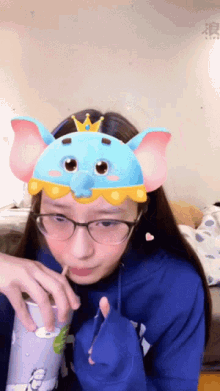 a girl wearing glasses and a blue elephant headband drinks from a cup