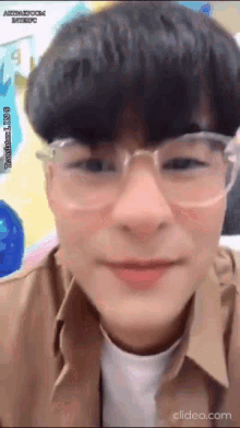 a young man wearing glasses and a brown shirt is looking at the camera .