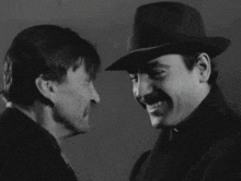 a man with a mustache is smiling next to another man in a hat