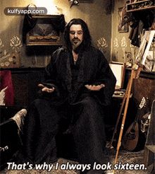 a man with long hair and a beard is sitting in a room with a cane and a cell phone .