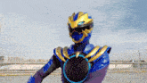 a blue and gold superhero with a black circle around his chest