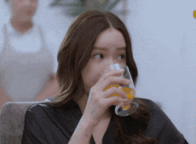 a woman is drinking a glass of orange juice while sitting on a couch