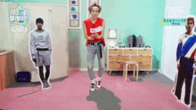 a man in a red tank top is dancing in a room with cardboard cutouts of other men .