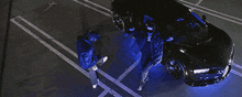 a couple of people standing next to a car with blue lights on it