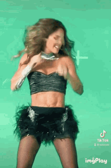 a woman in a black crop top and black skirt is dancing