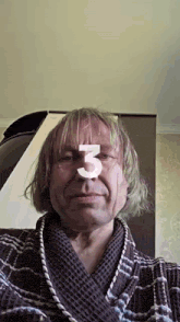 a man with blonde hair is wearing a robe and has the number 3 on his face .