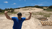 a man in a blue shirt is standing in the dirt with his arms outstretched