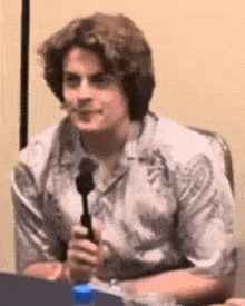 a man is sitting at a table holding a microphone and talking into it .