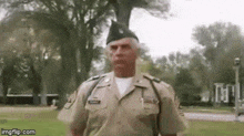 a man in a military uniform is standing in a grassy field with trees in the background .