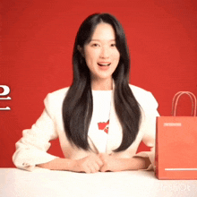 a woman in a white jacket is sitting at a table with a red bag in front of her that says inshot