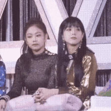 two women are sitting next to each other on a stage and looking at something .