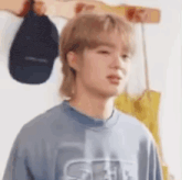 a young man with blonde hair is wearing a blue shirt and standing in front of a wall with hats hanging on it .