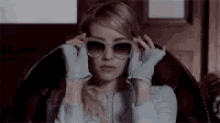 a woman is wearing gloves and sunglasses while sitting in a chair .