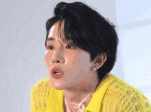 a close up of a person 's face with a yellow shirt and pearls