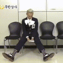 a man in a suit sits on the floor with his legs crossed in front of a wall with chinese writing on it