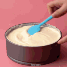 a person is using a blue spatula to stir a cake in a pan