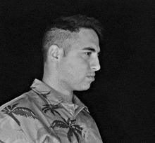 a man wearing a shirt with palm trees on it looks to the side