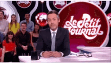 a man in a suit and tie stands in front of a le petit journal sign