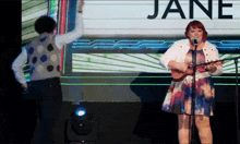 a woman singing into a microphone in front of a sign that reads jane