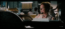 a woman wearing glasses and a headset is talking on a cell phone in an office .