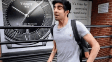 a man is walking in front of a tissot watch .