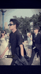 a man wearing sunglasses and a black shirt has a sticker on his shirt that says ' tb3 '