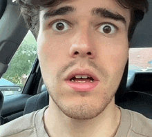 a man with a beard is making a surprised face in a car .