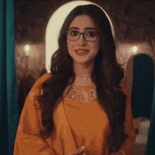 a woman wearing glasses and a yellow dress smiles at the camera