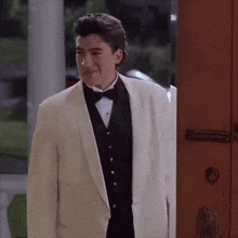 a man in a tuxedo and bow tie is standing in front of a door