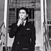 a man in a suit is smoking a cigarette while standing on stairs .