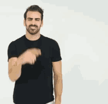 a man with a beard is wearing a black shirt and making a gesture with his hands