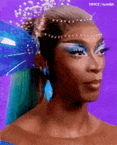 a close up of a woman 's face with blue makeup and a blue butterfly wing in her hair .