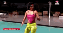 a woman in a pink top and yellow pants is dancing in front of a pool on tv .