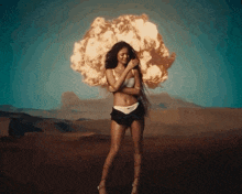 a woman in a bikini is standing in front of an explosion in the desert