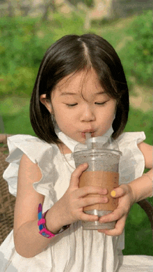a little girl in a white dress drinks from a cup with a straw