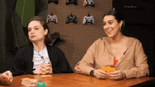 two women are sitting at a table playing a game and one of them is wearing a t-shirt that says games