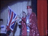 two men in red sequined outfits are holding a british flag on a stage .