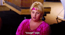 a woman is wearing a pink shirt and a pink headband and says `` cough slut '' .