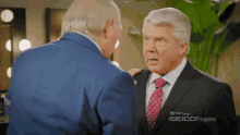two men in suits and ties are talking to each other in a room .