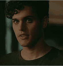 a close up of a man 's face with curly hair wearing a black shirt and looking at the camera .