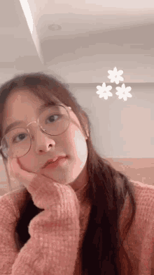 a young girl wearing glasses and a pink sweater looks at the camera
