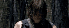 a man in a black tank top is standing in the woods with a sword .