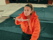 a woman in an orange jacket is standing on a street