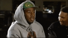a man wearing a hooded sweatshirt and a hat with the letter t on it