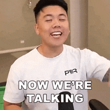 a man wearing a white t-shirt is smiling and says `` now we 're talking '' .
